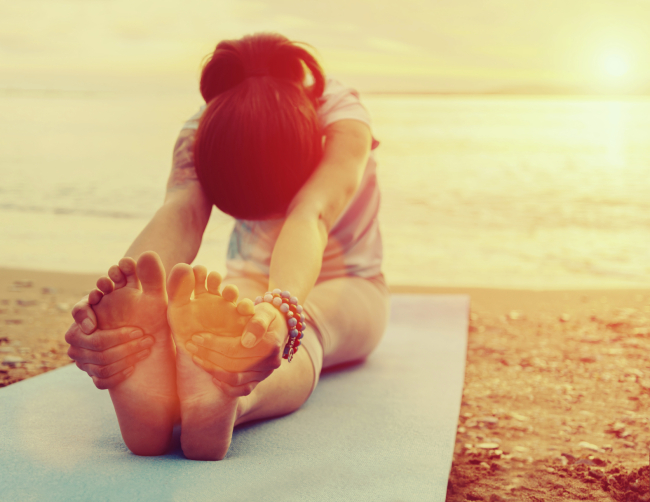Young woman doing yoga exercise on summer beach at sunset. Image with sunlight effect