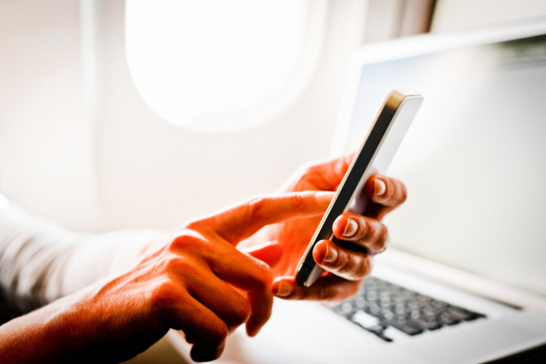 Woman using smartphone and laptop in airplane during flight