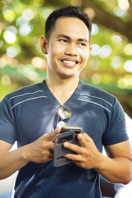 Happy Indonesian man portrait with sunglasses and phone, looking away. He is holding his mobile phone and smiling as if he just read good news. This attractive, healthy sportive man was photographed in Lovina, North Bali, Indonesia.