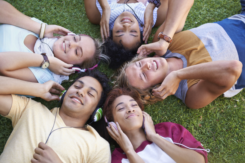 High angle of a group of friends lying on their backs on the grass in a park and listening to music