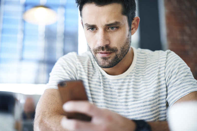 Shot of a handsome young man using his mobile phone while sitting at a restaurant table