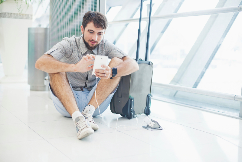 Man sitting next to airport outlet charging phone