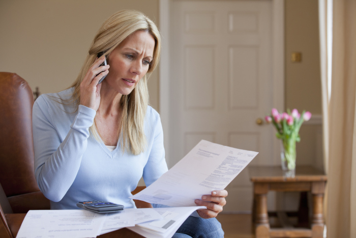 Concerned woman holding bills and talking on cell phone