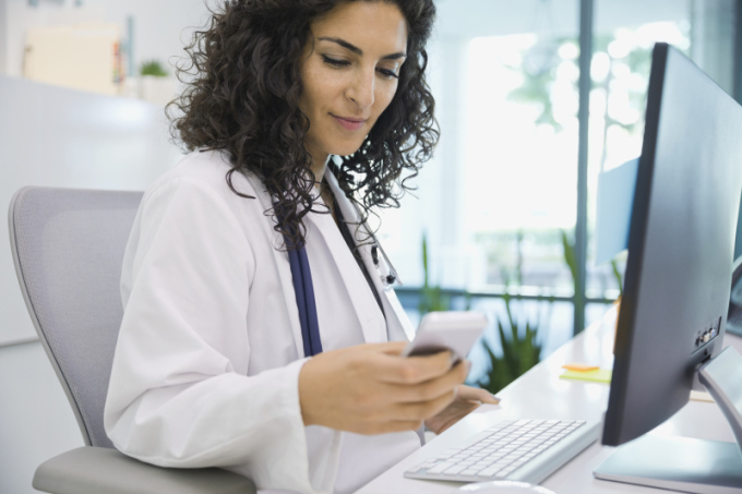 Female doctor sitting at desk using smart phone