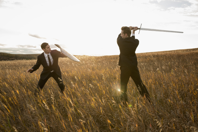 Angry businessmen fighting with sword and shield in field