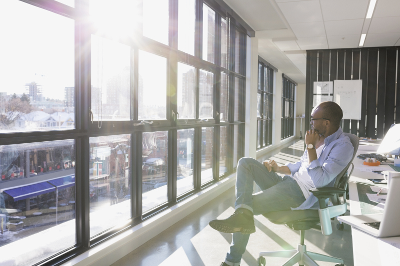 Pensive businessman looking out sunny office window