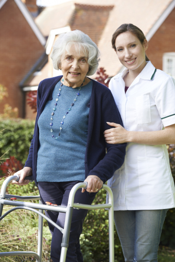 Carer Helping Senior Woman To Walk In Garden Using Walking Frame