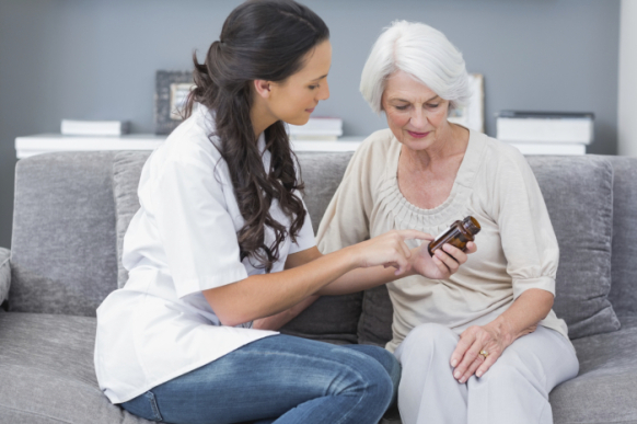 Doctor showing medication to her elderly patient on sofa