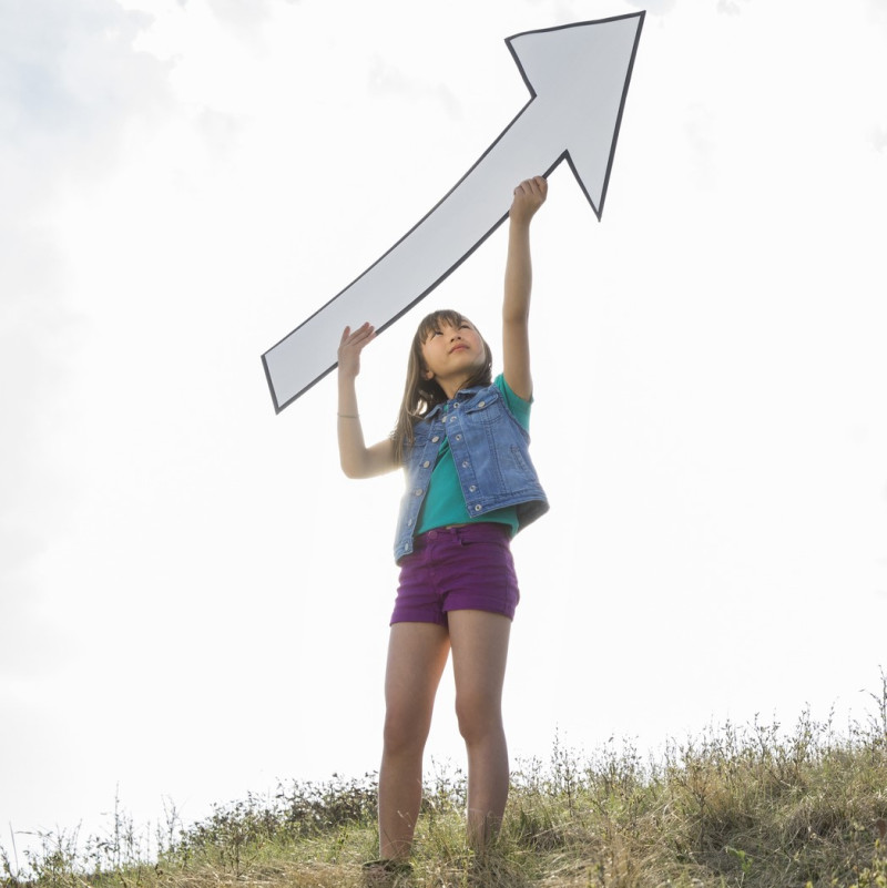 Schoolgirl holding upward arrow outdoors